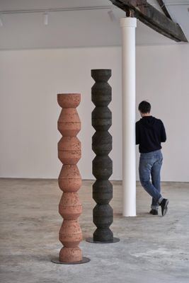 un homme debout dans une pièce, avec trois grands vases devant lui