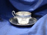 a silver cup and saucer sitting on a blue cloth