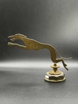 sculpture en laiton représentant un chien sautant par-dessus un socle posé sur une surface grise