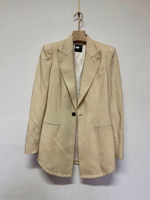 un blazer beige à fines rayures, suspendu à un cintre devant un mur blanc