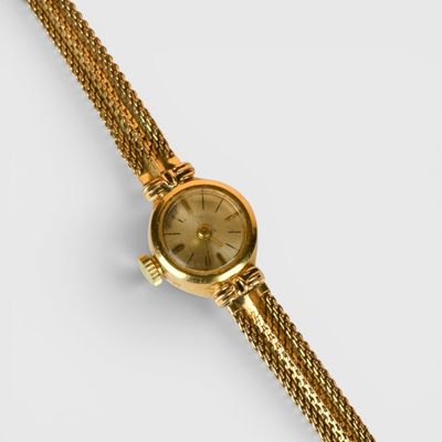 gros plan d'une montre en or sur une surface blanche