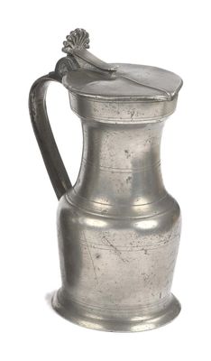 a silver pitcher with a spoon in it on a white surface