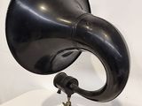 un gramophone noir posé sur un socle en bois, lui-même posé sur une table blanche