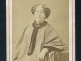 une vieille photo d'une femme assise sur une chaise, vêtue d'un châle