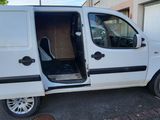une petite camionnette blanche dont la porte est ouverte, garée sur un parking