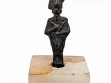 une image représentant une statue de femme coiffée d'un chapeau, posée sur un bloc de marbre