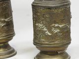 two brass vases sitting next to each other on a white surface
