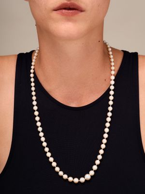 une femme vêtue d'un débardeur noir et d'un collier de perles