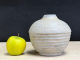a white vase sitting next to an apple on a table