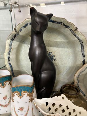 une statue de chat noir posée sur une table, à côté d'un bol