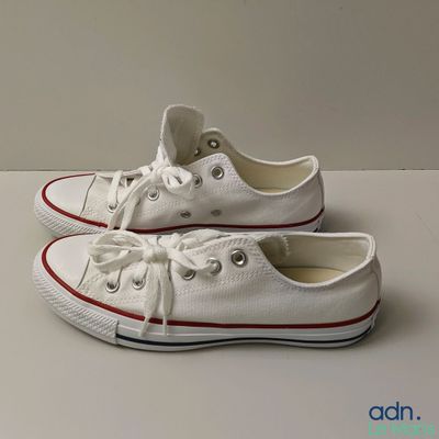Des baskets Converse blanches avec des lacets rouges sont posées sur une surface blanche