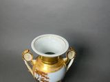 a gold and white vase on a stand on a gray surface