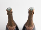 two bottles of champagne sitting next to each other on a white surface