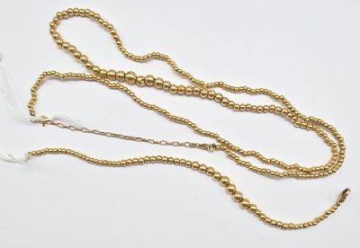 un gros plan d'un collier de perles dorées posé sur une surface blanche