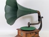 un vieux gramophone vert posé sur un support en bois, devant un fond blanc