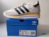 une paire de baskets Adidas blanches et noires posée sur une boîte bleue