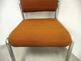 une chaise orange aux pieds chromés, dont l'assise est adossée au mur
