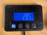 a digital clock on a table next to a cup of coffee