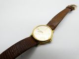 gros plan d'une montre sur une surface blanche avec un bracelet marron