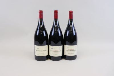 trois bouteilles de vin rouge sont alignées sur une surface blanche