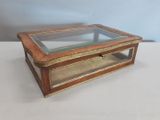 une vieille boîte en bois avec un couvercle en verre, posée sur une surface blanche