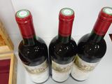 three bottles of red wine are lined up on a shelf