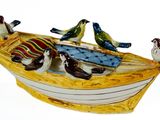 trois oiseaux perchés sur un petit bateau posé sur une surface blanche