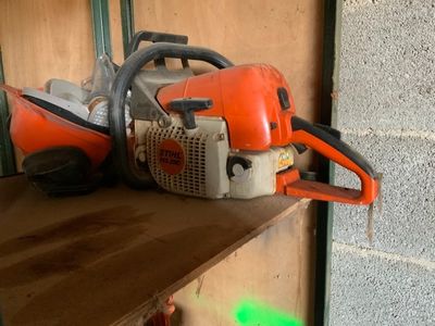 une tronçonneuse posée sur une étagère, à côté d'un mur de briques