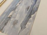 two framed pictures of watercolor paintings on a table with a gold frame