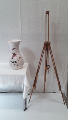 une table blanche sur laquelle se trouve un vase blanc, à côté d'un trépied