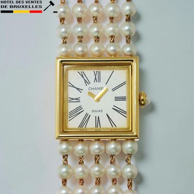 une montre en or avec des perles blanches, suspendue à une chaîne