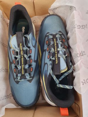 une paire de chaussures de course bleues et orange dans une boîte posée sur une table