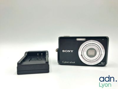 a black camera sitting next to a charger on a white surface