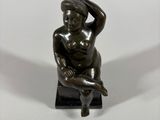 statue of a woman sitting on a stool with her hands on her head
