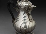 une cafetière ancienne en argent, avec une poignée noire sur un fond gris
