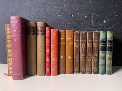 Plusieurs vieux livres sont alignés sur une étagère adossée à un mur noir