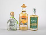 Trois bouteilles d'alcools de différentes sortes sont alignées sur une surface blanche