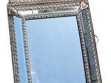 miroir argenté orné d'un motif décoratif sur le dessus, posé sur une surface blanche