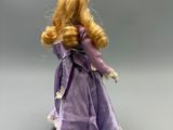 barbie doll with blonde hair and purple dress on a gray surface
