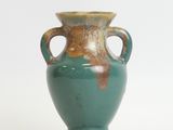 a green vase with two handles sitting on a white surface