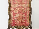 une chaise ancienne dont le dossier est recouvert d'un tissu rouge et or
