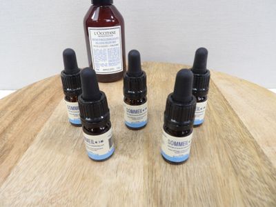 quatre flacons d'huiles essentielles posés sur une table en bois, à côté d'un flacon d'huile essentielle