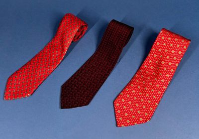 three ties are lined up on a blue surface, one red and one black
