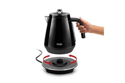 une personne tenant une bouilloire noire au-dessus d'une cafetière électrique