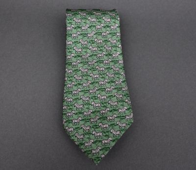La cravate est verte et blanche, avec un motif d'éléphants.