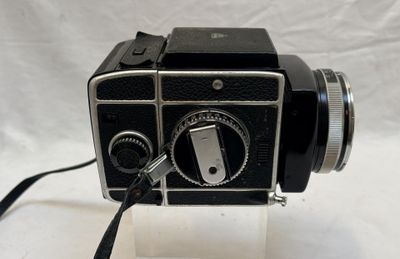 un appareil photo noir et argenté exposé sur une surface blanche