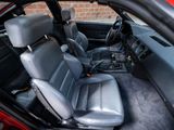 the interior of a red car with black leather seats and a red brick wall