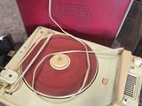 a record player sitting on top of a table next to a red suitcase