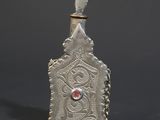 a small silver bottle with a red stone in it