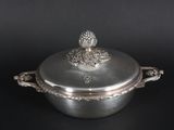 an antique silver plated casserole with a lid on a black background